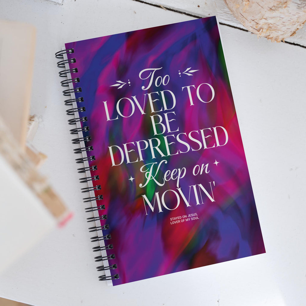 Too Loved to Be Depressed spiral notebook on a desk